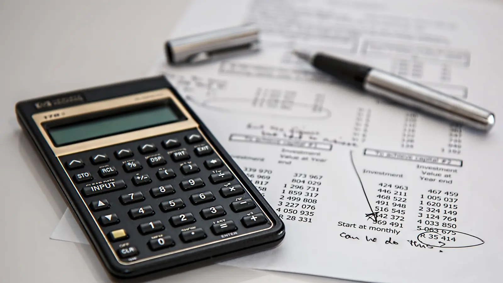 Printed financial statements on a desk with a black calculator and a ballpoint pen